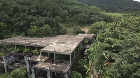 Aerial-backwards-dolly-shot-of-derelict-abandoned-building-on-a-tropical-island-with-palm-trees