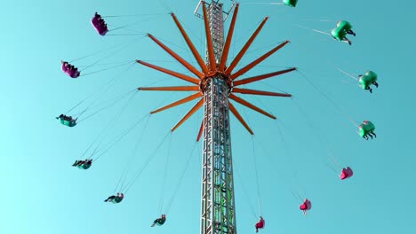 People-riding-vertical-chain-swing-ride-in-amusement-park,-tilt-up,-day