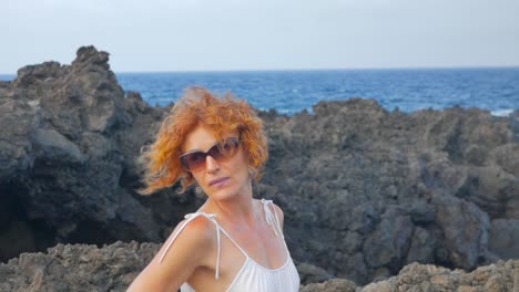 A-shot-of-a-redhead-woman-in-white-on-a-cliff-beside-the-ocean,-in-a-volcanic-island