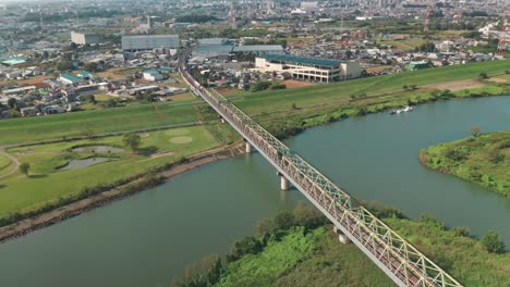 Fliegen-über-Den-Arakawa-fluss-Mit-Zügen,-Die-An-Der-Eisenbahnbrücke-Vorbeifahren,-Die-Die-Stadt-Fujimi-In-Saitama,-Japan,-überblickt