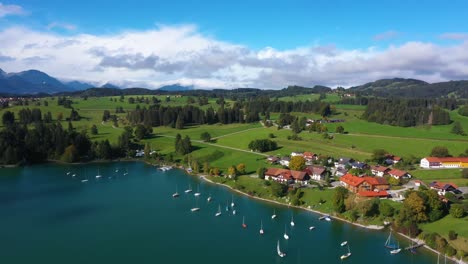 Amazing-aerial-view-descending-near-huge-lake-overlooking-small-village-with-boats-at-Forggensee-in-Bavaria,-Germany-in-4k