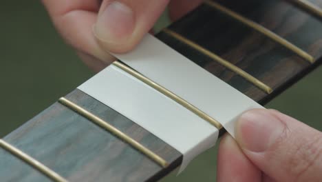 Man-Putting-Masking-Tape-On-The-Fingerboard-Of-An-Acoustic-Guitar-To-Protect-Before-Polishing-The-Frets