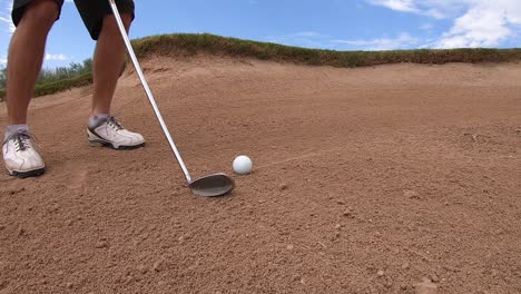 A-golfer-lines-up-the-sand-iron-behind-a-golfball-then-hits-it-out-of-the-sandtrap,-Scottsdale,-Arizona
