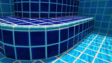 Underwater-footage-of-walking-along-the-bottom-of-a-swimming-pool-towards-steps-and-exiting