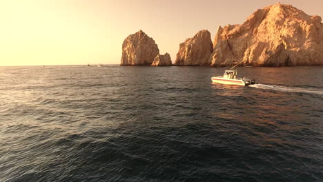 Drone-footage-at-Cabo-San-Lucas-Arch,-Mexico,-following-boat-cruising-along-water