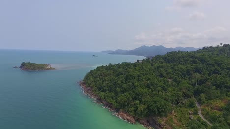 Tropical-Island-drone-trucking-left-shot-of-islands-with-lush-green-rain-forest-and-tropical-palm-trees-with-white-sand-beach-and-rocky-coastline