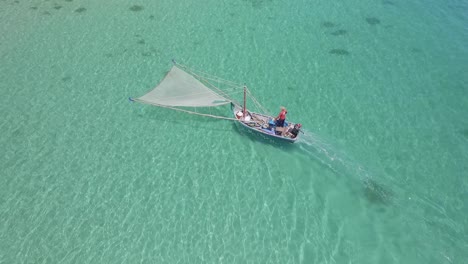 Aerial-shot-of-a-traditional-shrimp-fisherman-on-small-wooden-boat-fishing-for-shrimp-in-clear-waters-in-Thailand