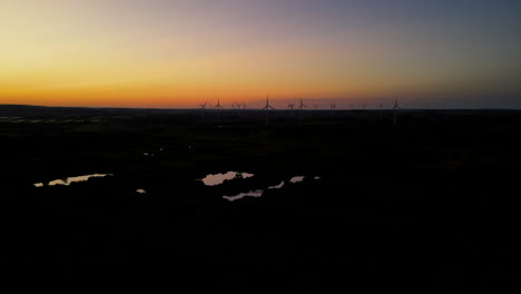 Windmills-overlooking-the-dark-landscape-during-twilight--aerial