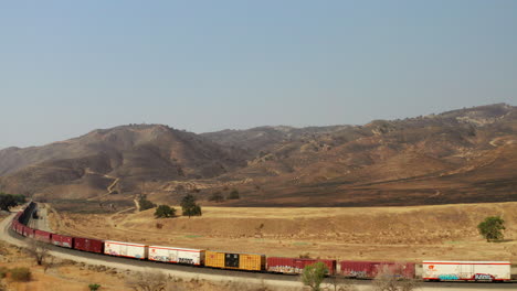 Stationary-train-on-the-tracks-beneath-hills-scorched-by-wildfires---aerial-view
