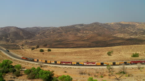 Train-rolls-along-the-tracks-beneath-the-site-of-a-large-wildfire-near-Caliente,-California---aerial-view