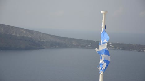 A-slightly-tattered-Greek-flag-blowing-in-the-breeze-in-Oia,-on-the-island-of-Santorini,-Greece