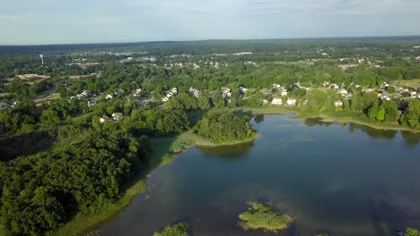 4k-Aerial-footage-of-a-small-lake-in-the-small-town-of-Oxford,-Michigan,-USA-moving-towards-a-suburban-residential-area-in-the-village-of-Oxford