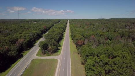 Clip-of-a-scenic-empty-rural-american-asphalt-highway-in-Michigan,-America-with-sunny-blue-sky-in-the-summer,-with-green-trees-all-around
