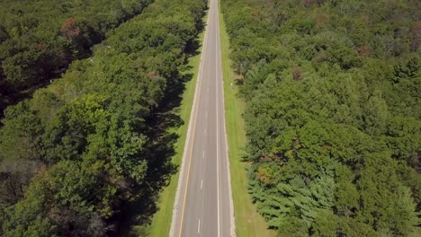 Daytime-clip-of-an-empty-michigan-asphalt-highway-in-rural-america,-in-sunny-summer-conditions-with-green-trees-and-scenic-aerial-view