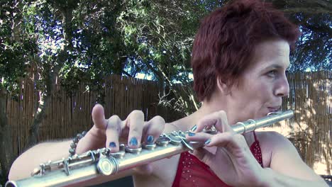 A-woman-in-a-red-dress-plays-a-tune-on-a-flute-outdoors,-close-up