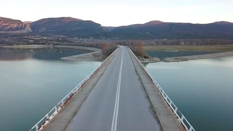 Drone shot of a girl riding towards the camera and passing under, on a  super sport motorcycle at a bridge over a lake in Greece