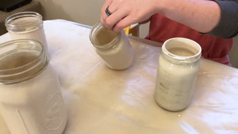 Camera-zooming-in-on-a-person-recycling-and-upcycling-mason-jars-by-painting-them-and-turning-them-into-vases