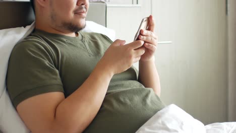 A-young-man-use-mobilephone-for-online-shopping,-chatting-on-the-bed-in-bedroom
