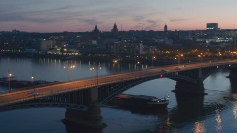 sunset-aerial-drone-shot-of-city-of-Mainz-by-night-with-a-drone-over-the-old-bridge-and-a-ship-on-the-rhine-river-Luftaufnahmen-per-Drohne