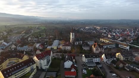 View-of-the-church-of-the-village-of-Denzlingen,-cemetery-in-the-background,-a-train-is-leaving