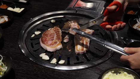 Samgyeopsal---Person-Cutting-Grilled-Pork-Belly-With-Scissors-Over-Charcoal-Griller-In-Korean-Restaurant