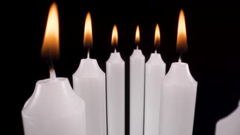 macro-view-flying-past-lit-candles-on-black-background,-moving-past-white-candles