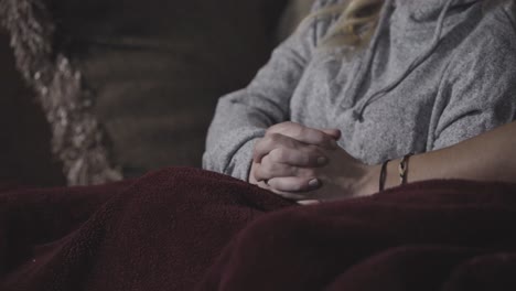 A-young-couple-watching-TV-holds-hands-while-cuddling-under-a-blanket-together
