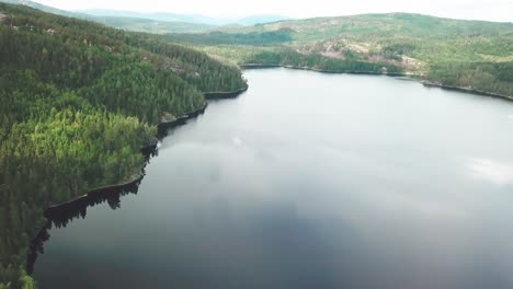 Sideways-movement-of-a-aerial-shot-with-slight-tilt-down-over-a-lake-surrounded-by-a-forest
