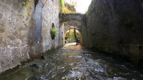 Flight-of-the-FPV-drone-over-a-river-and-passing-over-the-stone-arches-of-an-ancient-ammunition-factory-in-Eugi