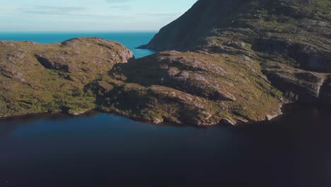 Panning,-tilt-down-drone-shot-of-a-rocky-hill-over-a-lake-in-south-Lofoten
