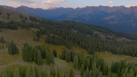 Aerial-flying-over-trees-on-a-ridge-and-towards-mountain-peaks-in-the-Colorado-Rockies-on-a-beautiful-summer-day-at-golden-hour