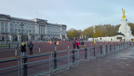 Pan-shot-of-local-and-international-visitors-in-front-of-Buckingham-Palace,-London,-UK,-with-view-of-a-grass-garden-in-front-at-daytime