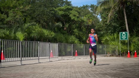 Slow-motion-of-a-teenage-athlete-wearing-a-pink-and-blue-suit-running-the-final-stage-of-a-triathlon-competition-looking-concentrated-and-tired