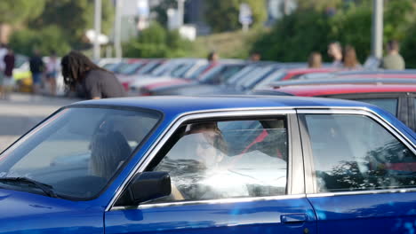 Fan-club-car-meeting-of-BMW-e30,-telephoto-shot-of-couple-driving-blue-vehicle