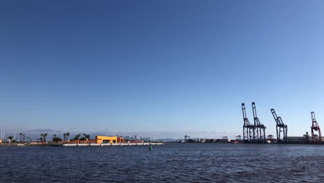 Slow-Motion-Clip-of-an-industrial-dock-harbor-with-industrial-containers-and-cranes-on-the-background-and-a-beautiful-blue-sky-with-some-seagulls-and-the-sea-with-waves