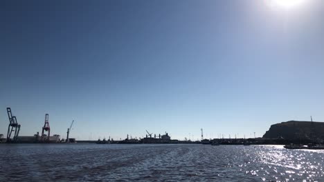 Slow-Motion-Clip-of-an-industrial-dock-harbor-with-containers-and-cranes-on-the-background-and-a-beautiful-blue-sky-with-some-seagulls-and-the-sea-with-waves