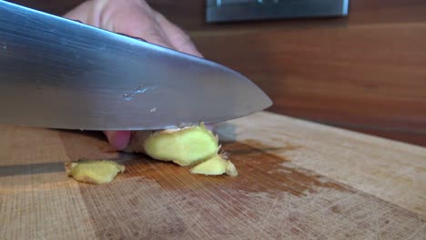 Ginger-root-being-cut-into-little-pieces-with-a-big-knife-on-a-wooden-cutting-board