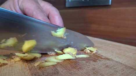 Pieces-of-ginger-being-cut-into-smaller-pieces-with-a-big-knife-on-a-wooden-cutting-board