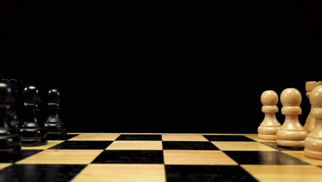 Dolly-shot-backwards-along-the-chess-pieces-standing-on-either-side-of-the-chessboard-against-a-black-background