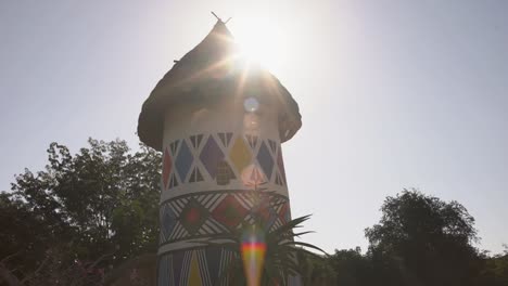 Bewegende-Aufnahme-Von-Ndebele-Mustern-Auf-Der-Hütte,-Im-Hintergrund-Bewegt-Sich-Die-Sonne-Am-Dach-Vorbei