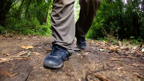A-man-walking-in-the-jungle,-camera-focused-on-his-legs,-showing-him-stepping-forward-on-the-dirt-road-with-his-shoes-framed