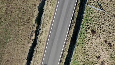 Top-down-shot-of-a-car-passing-through-frame-on-a-rural-road-in-Derbyshire,-UK