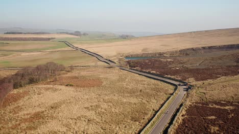 Chasing-a-car-and-a-cyclist-along-a-moorland-road-in-Derbyshire,-UK-with-a-drone
