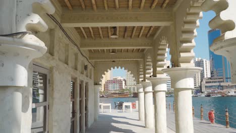 Revealing-Shot-Of-A-Woman-Walking-On-Promenade-By-Waterfront-Building-With-Arabesque-Arches-In-Al-Fahidi-Neighborhood---tilt-down