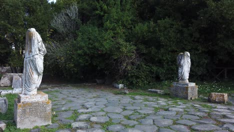 2-roman-statues-on-each-side-of-a-roman-road-in-Ostia-antica,-a-world-famous-archaeological-site-of-ancient-Rome