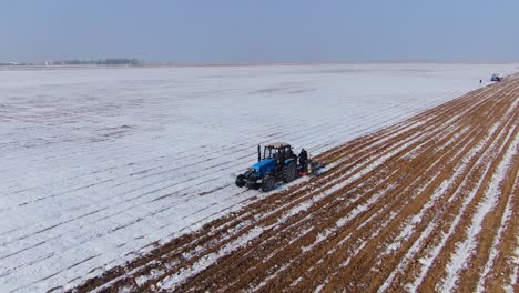 Blauer-Traktor,-Der-Im-Winter-Auf-Dem-Feld-Mit-Schnee-Pflügt-Und-Sät