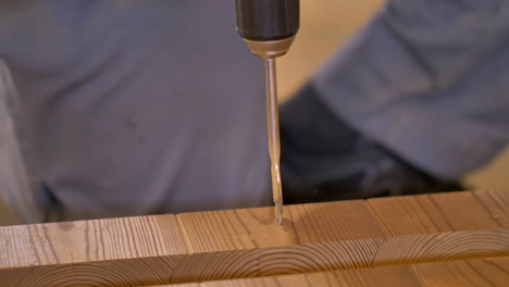 Wood-worker-drills-a-hole-with-paddle-bit-attached-to-hand-drill-in-thermo-pine-material