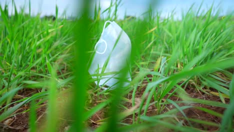 Medical-protective-face-mask-discarded-on-green-grass,-blown-by-strong-wind,-nature-pollution-during-the-Coronavirus-Covid-19-pandemic