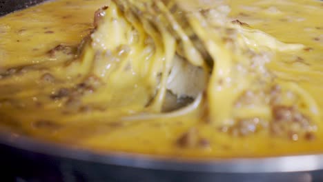Close-up-cooking-eggs-with-sausage-chunks-in-stainless-pan-on-stovetop-in-slow-motion