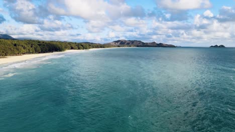 drone-video-of-beautiful-lucious-water-off-waimanalo-oahu-hawaii-deep-blues-of-ocean-with-white-sand-beach-midday-sunny-tropical-paradise-with-islands-off-in-background-panning-up-to-open-to-view